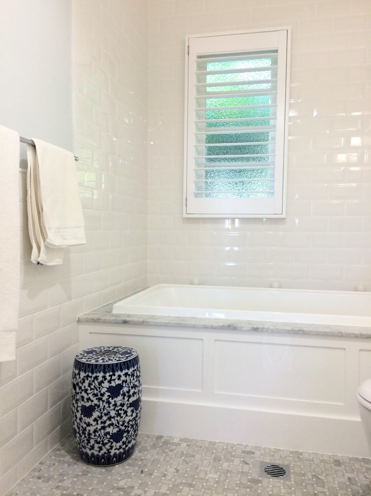 Klassisk inredning av ett mellanstort en-suite badrum, med luckor med infälld panel, vita skåp, ett platsbyggt badkar, en dusch/badkar-kombination, en toalettstol med hel cisternkåpa, vit kakel, tunnelbanekakel, grå väggar, klinkergolv i keramik, ett undermonterad handfat, marmorbänkskiva och grått golv