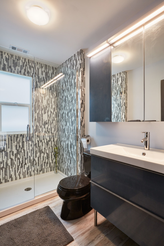 На фото: ванная комната среднего размера в современном стиле с плоскими фасадами, серыми фасадами, душем в нише, раздельным унитазом, черной плиткой, черно-белой плиткой, серой плиткой, белой плиткой, удлиненной плиткой, серыми стенами, полом из ламината, душевой кабиной, монолитной раковиной, столешницей из искусственного камня, бежевым полом и душем с распашными дверями с