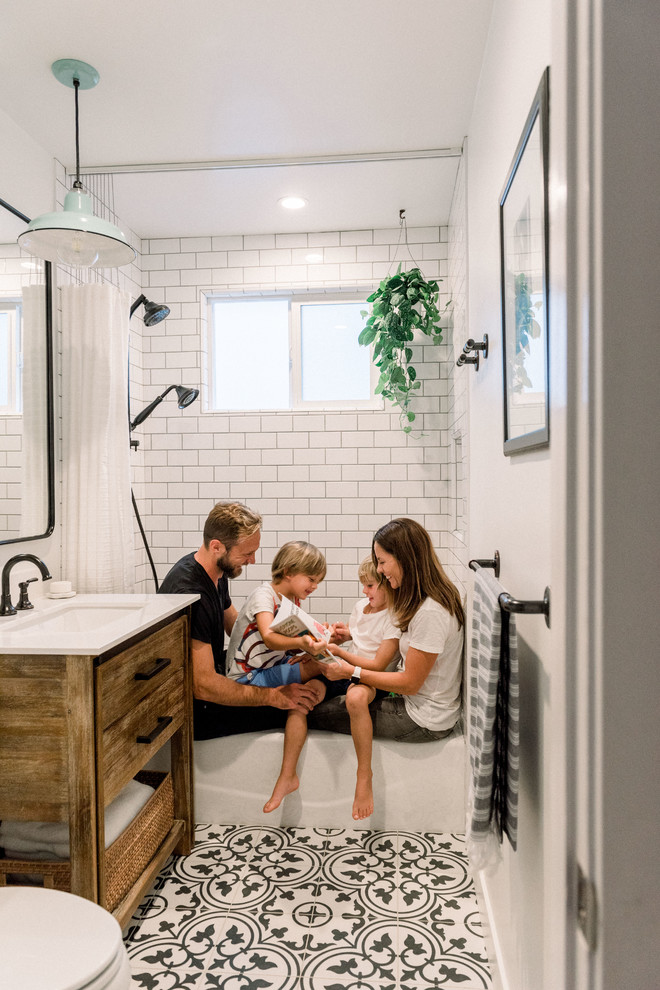 This is an example of a small country family bathroom in San Diego with flat-panel cabinets, medium wood cabinets, a corner bath, an alcove shower, a two-piece toilet, white tiles, metro tiles, white walls, porcelain flooring, a console sink, engineered stone worktops, black floors, a shower curtain and white worktops.