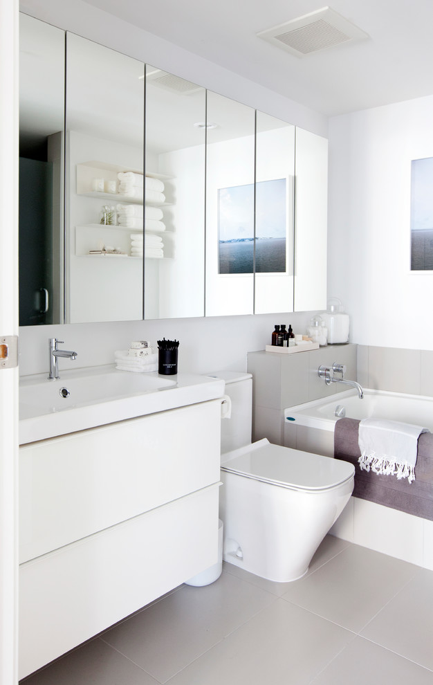 Photo of a small scandi ensuite bathroom in Vancouver with an integrated sink, flat-panel cabinets, white cabinets, a built-in bath, an alcove shower, a one-piece toilet, grey tiles, porcelain tiles, white walls and porcelain flooring.