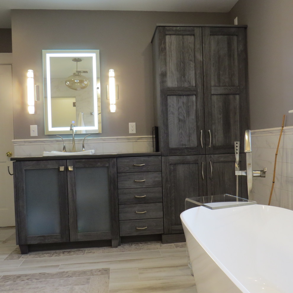 Large contemporary ensuite bathroom in Portland Maine with glass-front cabinets, grey cabinets, a freestanding bath, a built-in shower, a wall mounted toilet, multi-coloured tiles, porcelain tiles, grey walls, porcelain flooring, a built-in sink, engineered stone worktops, multi-coloured floors and a hinged door.