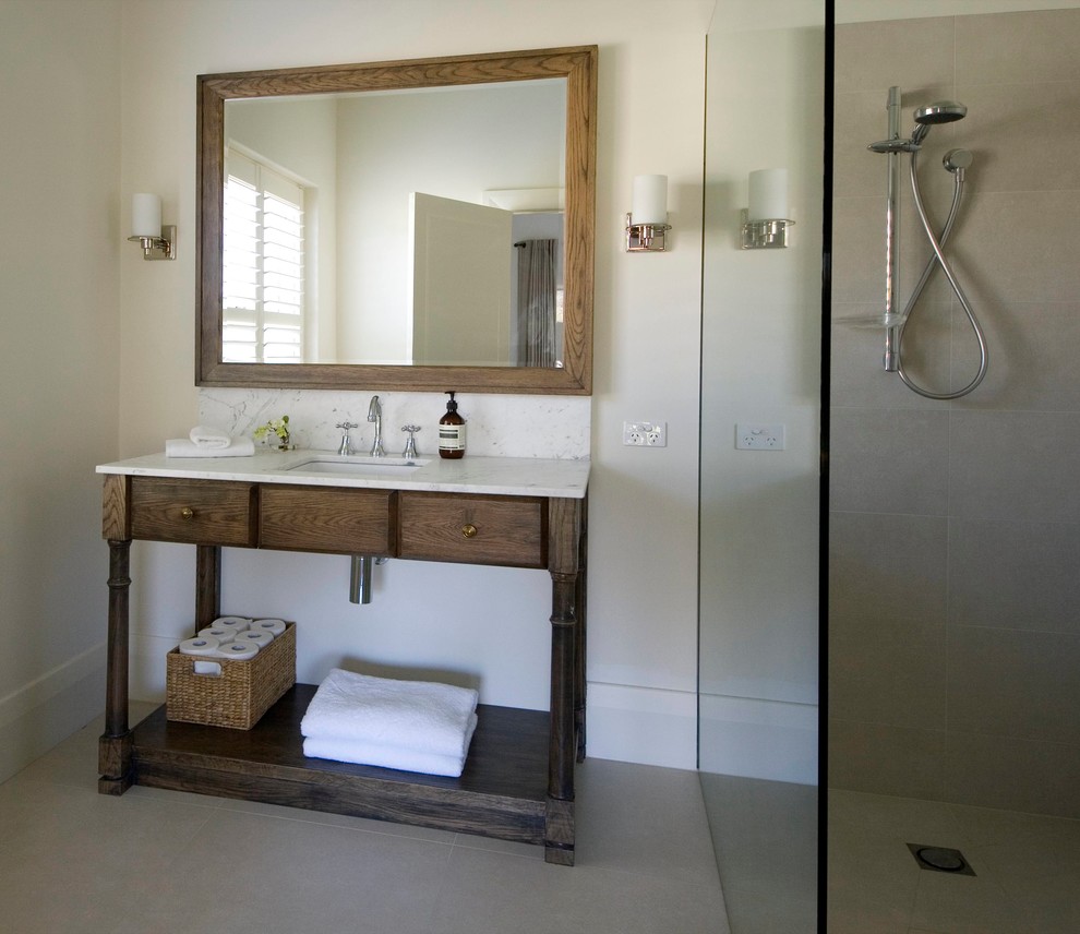 Diseño de cuarto de baño clásico de tamaño medio con lavabo bajoencimera, puertas de armario de madera oscura, encimera de mármol, paredes beige, ducha abierta y armarios tipo mueble