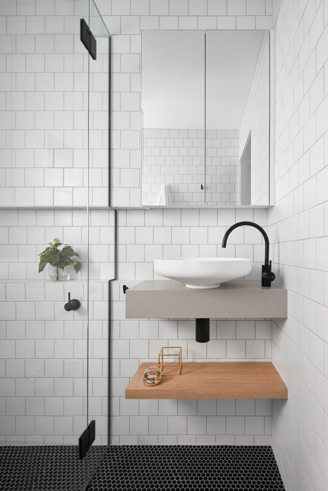 Exempel på ett litet minimalistiskt badrum, med öppna hyllor, skåp i ljust trä, en kantlös dusch, vit kakel, tunnelbanekakel, vita väggar, mosaikgolv, ett väggmonterat handfat, dusch med gångjärnsdörr och bänkskiva i akrylsten