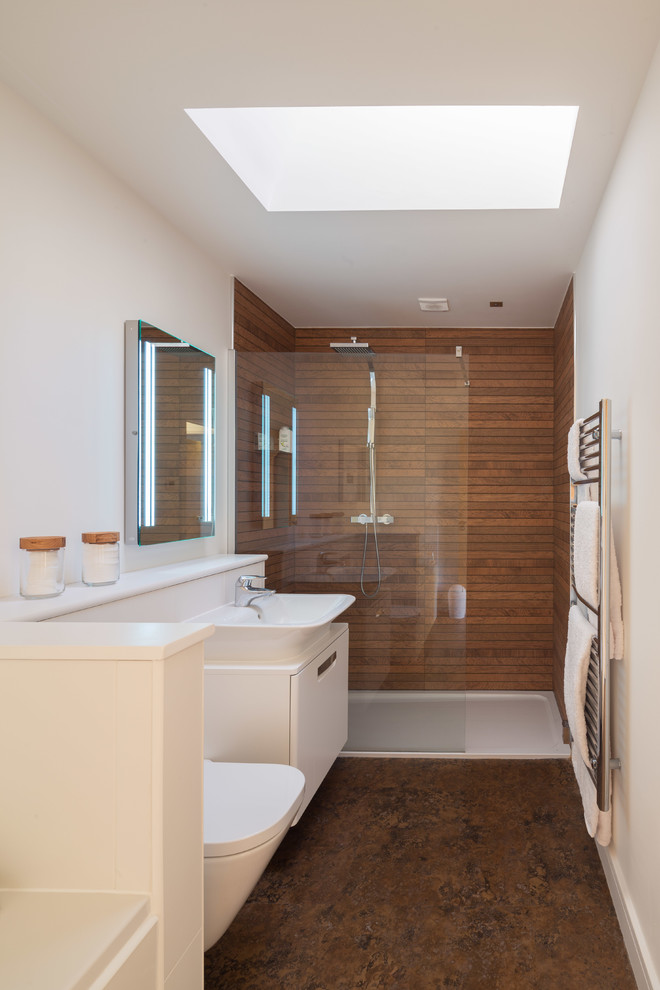 Photo of a small contemporary family bathroom in Cambridgeshire with flat-panel cabinets, white cabinets, a built-in bath, a walk-in shower, a wall mounted toilet, brown tiles, ceramic tiles, white walls, vinyl flooring, a console sink, wooden worktops, brown floors and an open shower.