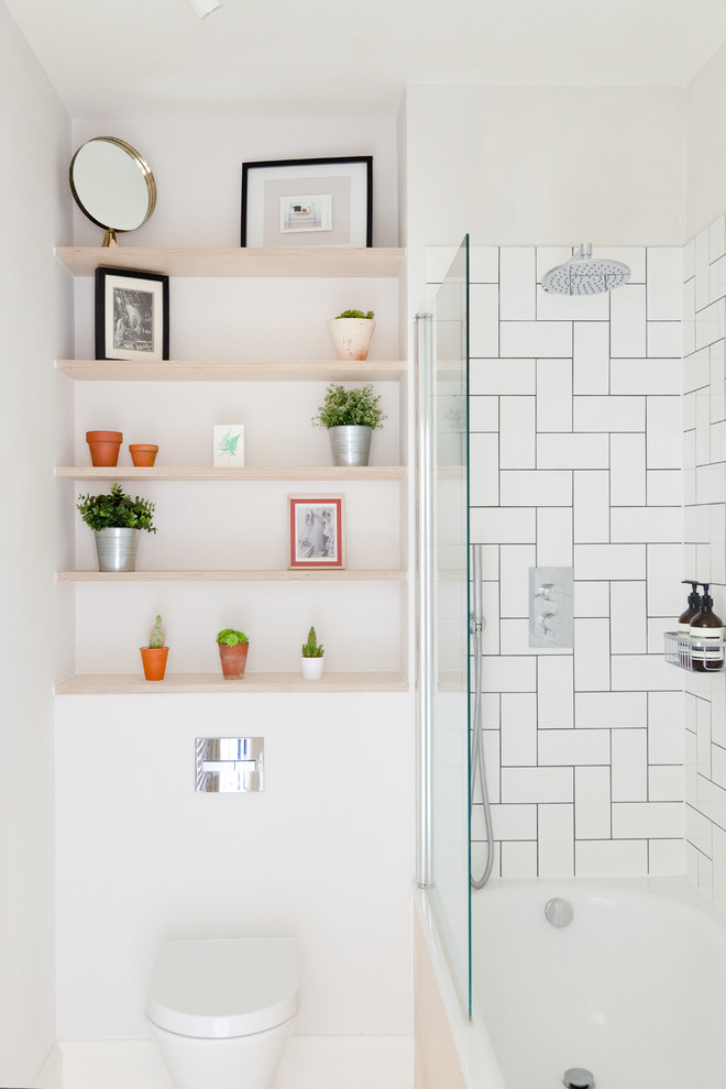 Photo of a contemporary bathroom in London with flat-panel cabinets, light wood cabinets, a built-in bath, a shower/bath combination, white tiles, ceramic tiles and white walls.
