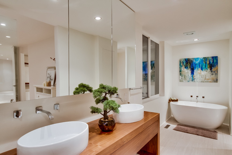 Cette photo montre une salle de bain tendance avec une vasque, une baignoire indépendante, un mur blanc et un plan de toilette en bois.