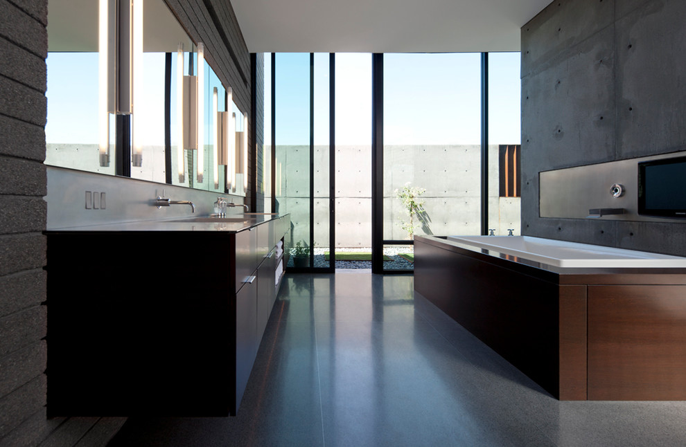 Пример оригинального дизайна: главная ванная комната в стиле модернизм с плоскими фасадами, фасадами цвета дерева среднего тона, полновстраиваемой ванной, открытым душем, серыми стенами, бетонным полом, монолитной раковиной и столешницей из нержавеющей стали