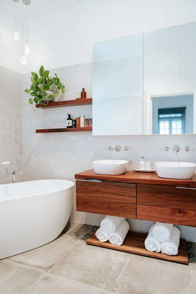 Bild på ett industriellt en-suite badrum, med skåp i mellenmörkt trä, ett fristående badkar, grå kakel, keramikplattor, cementgolv och träbänkskiva