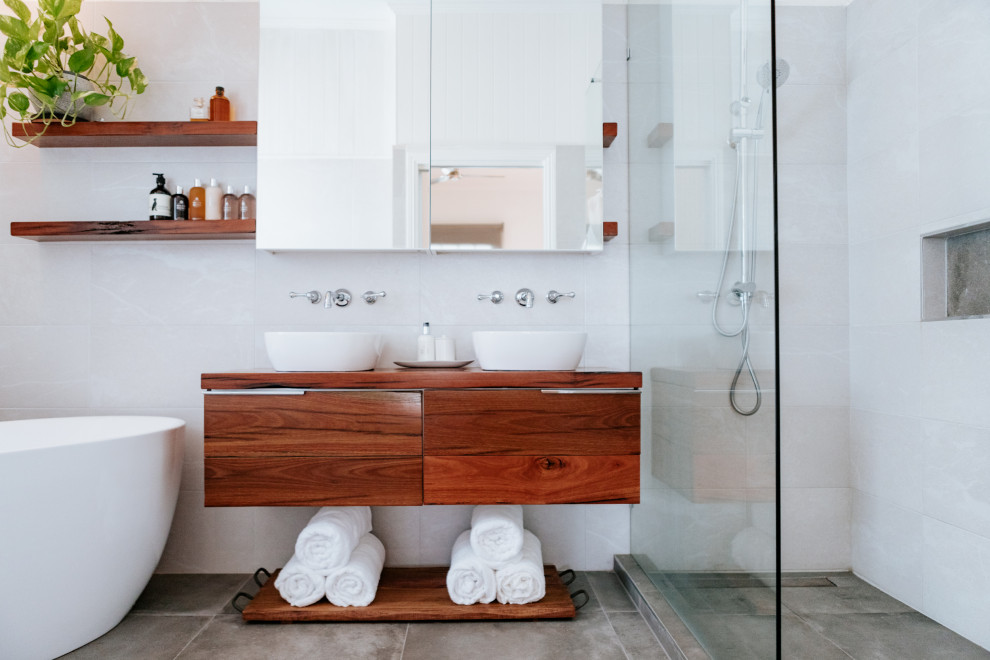 Inspiration for an industrial ensuite bathroom in Brisbane with medium wood cabinets, a freestanding bath, grey tiles, ceramic tiles, cement flooring and wooden worktops.