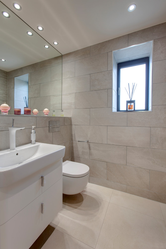 Modern inredning av ett en-suite badrum, med släta luckor, vita skåp, en vägghängd toalettstol, beige kakel, porslinskakel, klinkergolv i porslin, ett nedsänkt handfat och kaklad bänkskiva