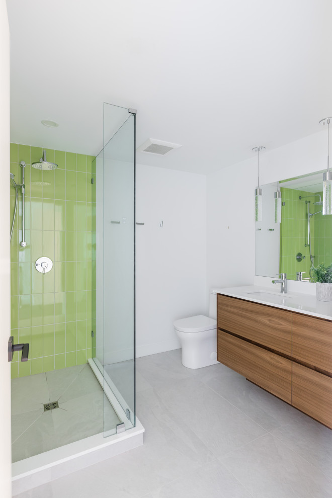 Inspiration for a medium sized modern ensuite bathroom in Vancouver with flat-panel cabinets, medium wood cabinets, double sinks, a built in vanity unit, a corner shower, a one-piece toilet, green tiles, metro tiles, white walls, porcelain flooring, a submerged sink, quartz worktops, grey floors, a hinged door and white worktops.
