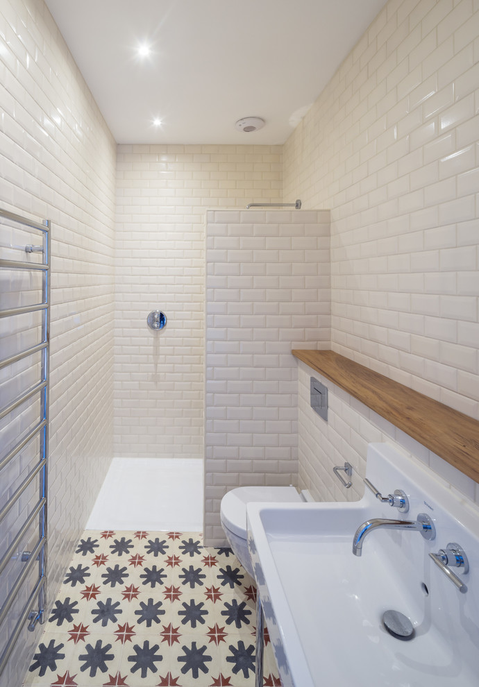Urban ensuite bathroom in London with a walk-in shower, a wall mounted toilet, white tiles, ceramic tiles, white walls, mosaic tile flooring and a pedestal sink.