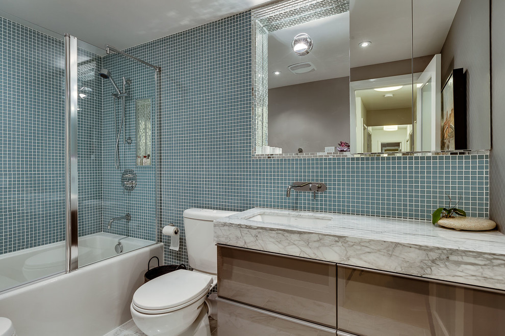 Esempio di una piccola stanza da bagno moderna con lavabo sottopiano, ante lisce, ante grigie, top in marmo, vasca da incasso, WC a due pezzi, piastrelle blu, piastrelle di vetro, pareti grigie e pavimento in marmo