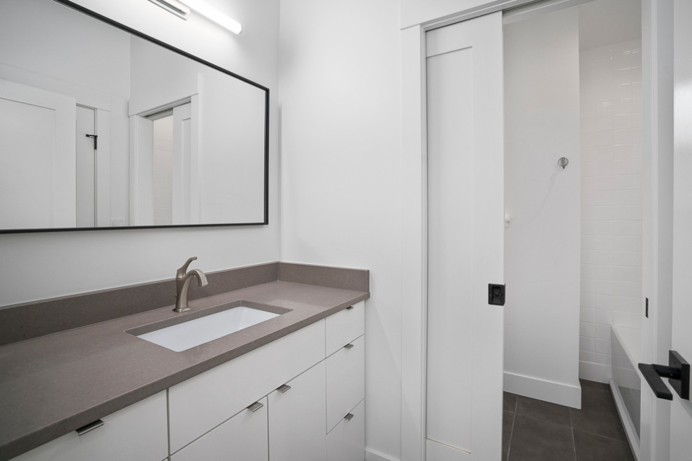 Design ideas for a medium sized traditional bathroom in Albuquerque with flat-panel cabinets, white cabinets, an alcove bath, a shower/bath combination, a two-piece toilet, white tiles, ceramic tiles, white walls, porcelain flooring, a submerged sink, engineered stone worktops, grey floors, a shower curtain and grey worktops.