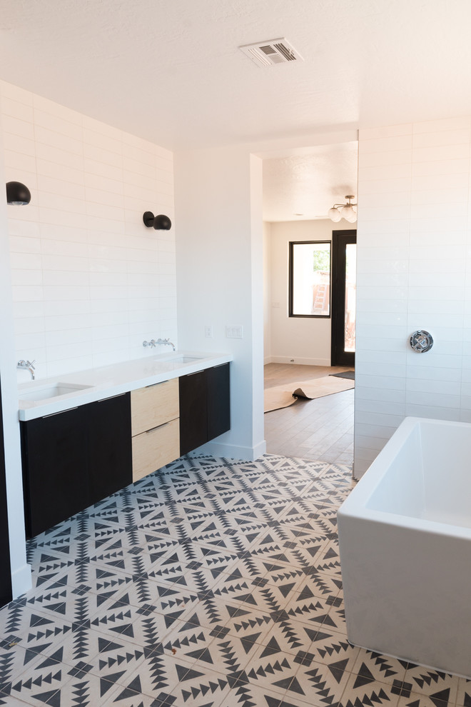 Inspiration pour une grande salle de bain principale design avec un carrelage blanc, carreaux de ciment au sol, un sol noir, un placard à porte plane, des portes de placard noires, une baignoire indépendante, un mur blanc et un lavabo encastré.