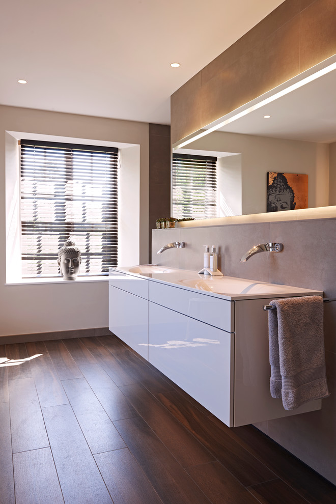 Inspiration for a medium sized contemporary ensuite bathroom in Devon with a wall-mounted sink, flat-panel cabinets, white cabinets, a freestanding bath, a walk-in shower, a wall mounted toilet, grey tiles, porcelain tiles, grey walls and porcelain flooring.