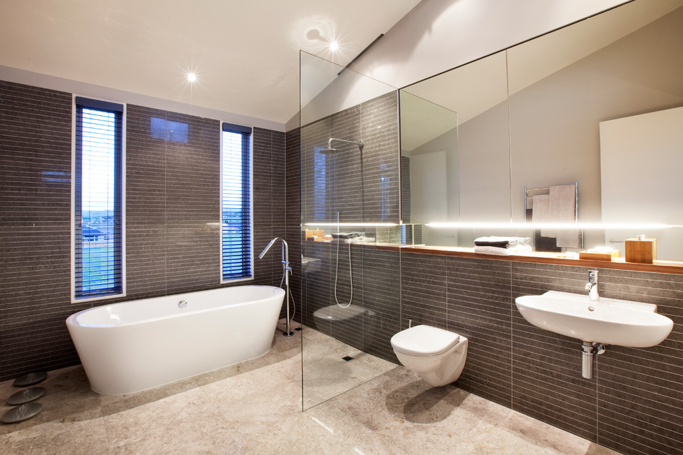 Modelo de cuarto de baño actual con bañera exenta, ducha abierta, sanitario de pared, baldosas y/o azulejos marrones, lavabo suspendido y ducha abierta