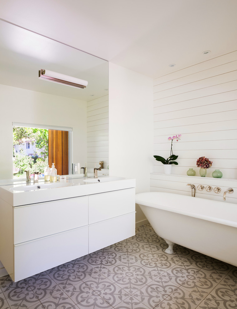 Foto på ett mellanstort funkis en-suite badrum, med släta luckor, vita skåp, ett fristående badkar, vit kakel, vita väggar, klinkergolv i porslin och ett integrerad handfat