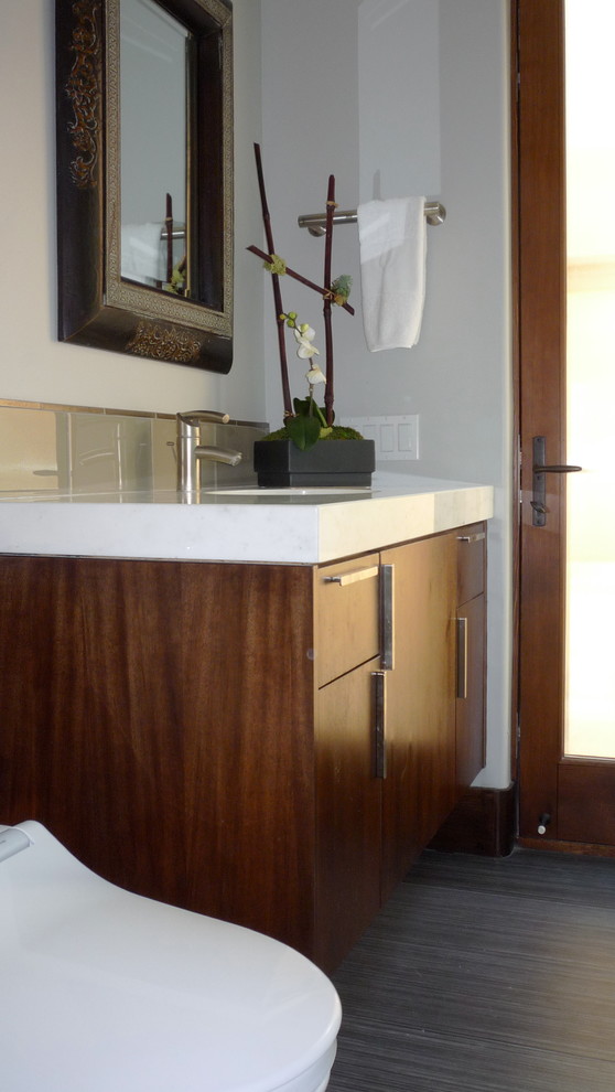 Immagine di una piccola stanza da bagno minimal con lavabo sottopiano, ante lisce, ante in legno bruno, top in marmo, doccia ad angolo, piastrelle grigie, piastrelle di vetro, pareti grigie e pavimento in gres porcellanato