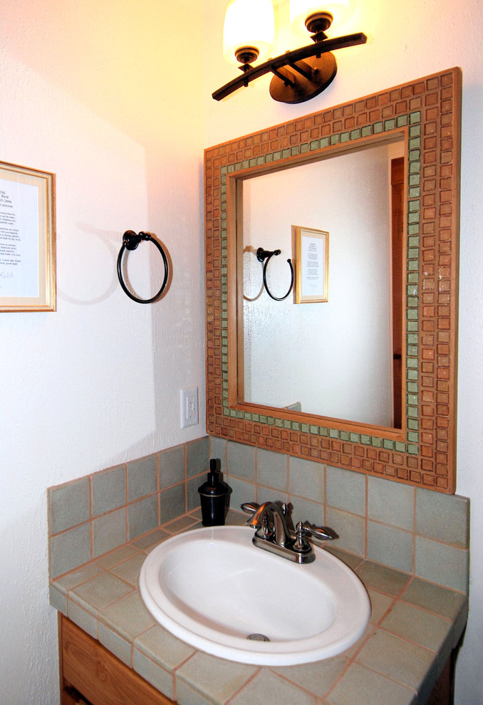 Cette image montre une petite salle d'eau sud-ouest américain en bois brun avec un placard à porte plane, un lavabo posé, WC à poser, un carrelage gris, un mur blanc et un plan de toilette en carrelage.