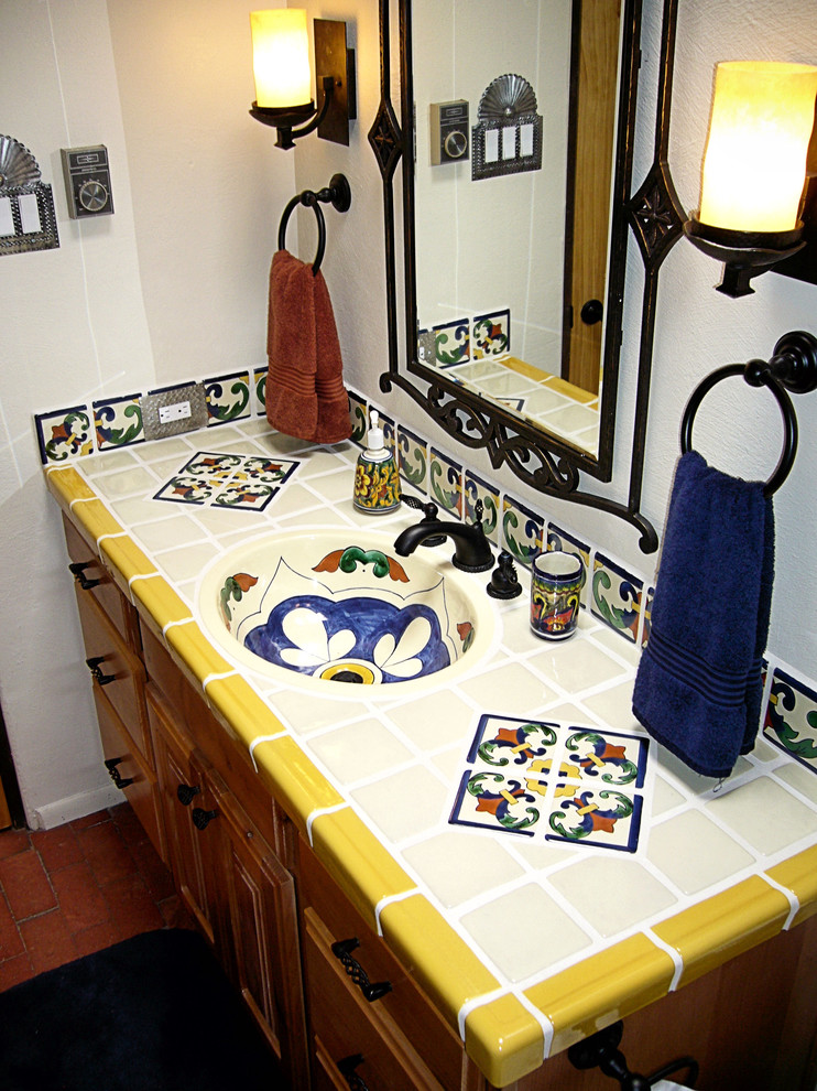 Réalisation d'une salle de bain tradition en bois clair de taille moyenne avec un placard avec porte à panneau surélevé, WC à poser, un carrelage bleu, un carrelage blanc, un carrelage jaune, des carreaux de céramique, un mur blanc, un sol en brique, un lavabo intégré, un plan de toilette en carrelage, un sol rouge et une cabine de douche avec un rideau.