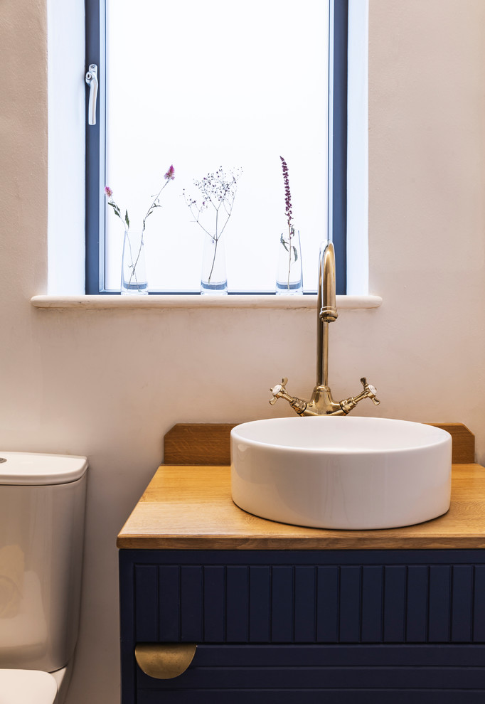 Ejemplo de cuarto de baño principal tradicional renovado con puertas de armario azules, paredes blancas y encimera de madera