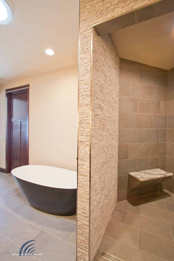 Cette photo montre une grande salle de bain principale moderne avec une baignoire indépendante, une douche à l'italienne, un carrelage beige, un carrelage de pierre, un mur beige, un sol en carrelage de porcelaine, un sol beige et un banc de douche.