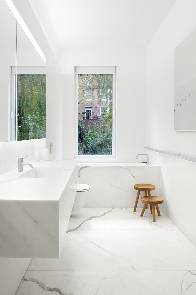 Idee per una stanza da bagno padronale moderna di medie dimensioni con WC sospeso, pareti bianche, pavimento in marmo, lavabo integrato, top in marmo, vasca ad alcova e piastrelle di marmo