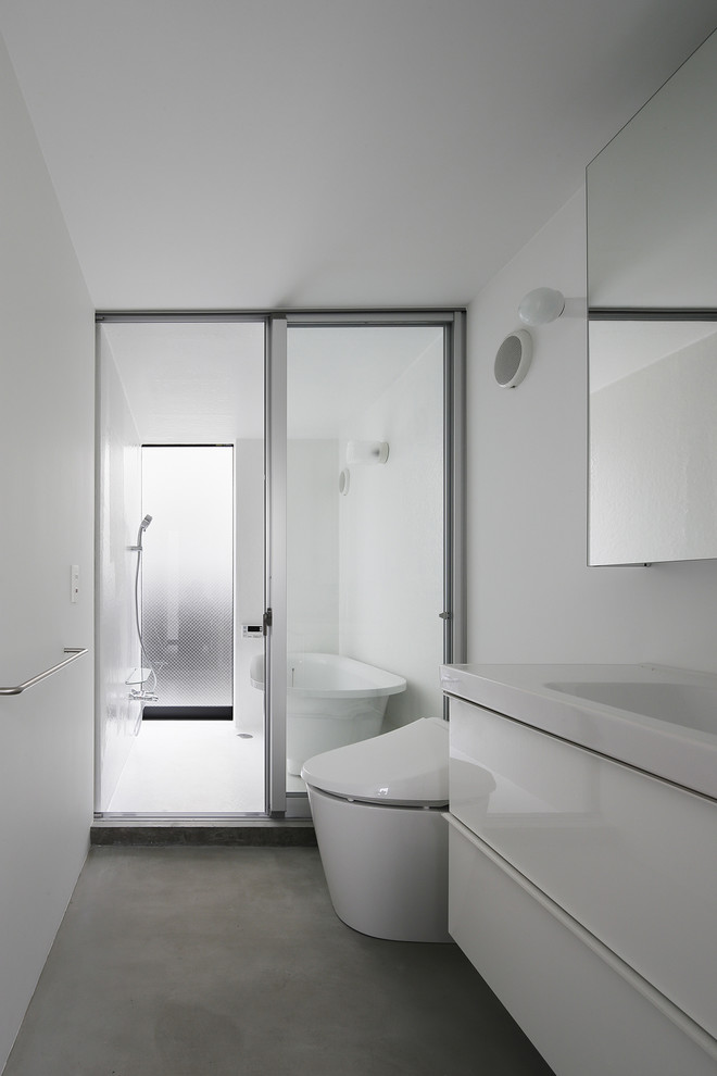 Foto på ett litet funkis vit en-suite badrum, med släta luckor, vita skåp, ett fristående badkar, en öppen dusch, en toalettstol med hel cisternkåpa, vita väggar, betonggolv, ett integrerad handfat och grått golv