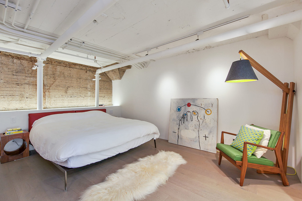 Modelo de dormitorio urbano sin chimenea con paredes blancas, suelo de madera clara y suelo beige