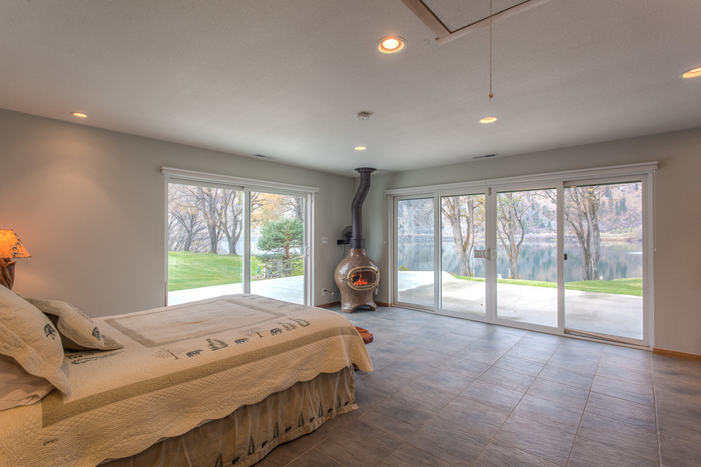 Imagen de habitación de invitados costera de tamaño medio con paredes grises, suelo de baldosas de cerámica, estufa de leña y suelo gris