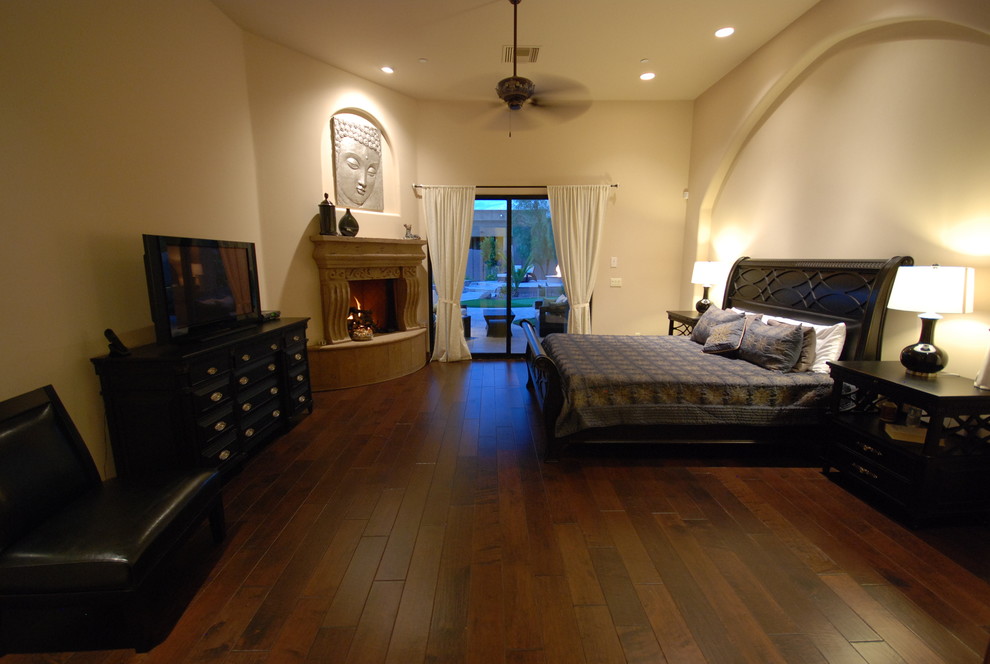 Inspiration for a large mediterranean master dark wood floor bedroom remodel in Phoenix with beige walls, a corner fireplace and a stone fireplace