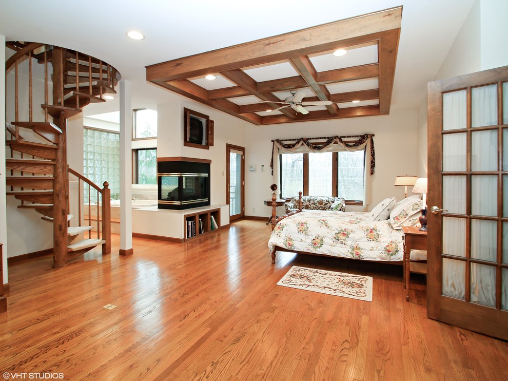Imagen de dormitorio tradicional con paredes blancas, suelo de madera en tonos medios y chimenea de doble cara