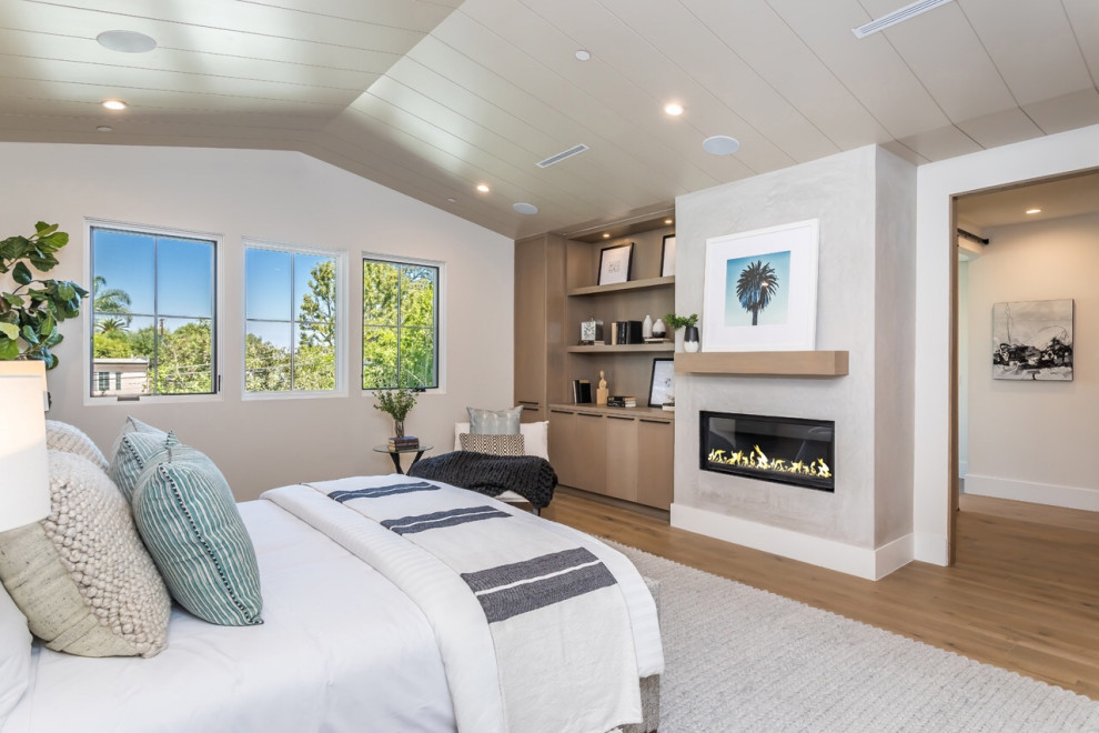 Large country master bedroom with beige walls, light hardwood flooring, a ribbon fireplace, a concrete fireplace surround and beige floors.