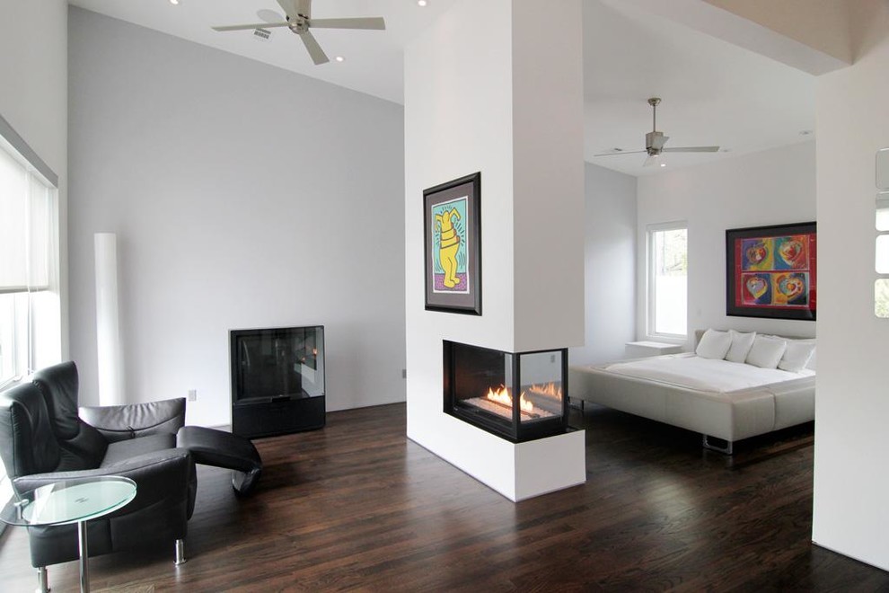 Photo of a contemporary master bedroom in Houston with a two-sided fireplace, white walls and dark hardwood flooring.