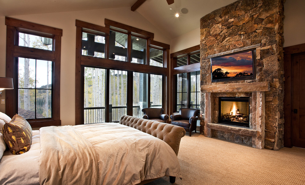 На фото: спальня в стиле рустика с ковровым покрытием, стандартным камином, фасадом камина из камня и телевизором