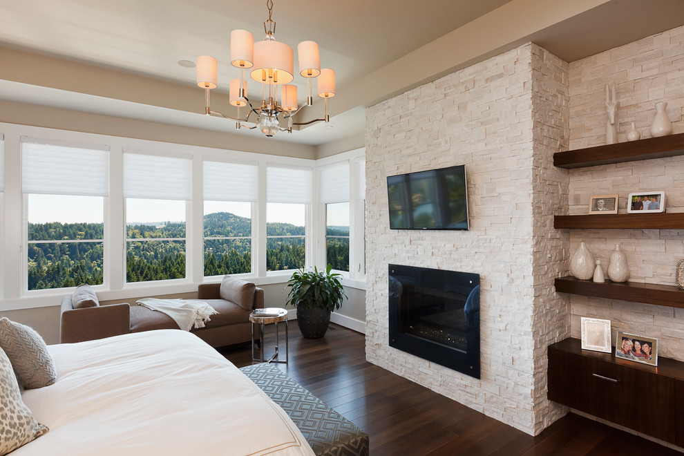 Cette photo montre une grande chambre parentale tendance avec un mur beige, parquet foncé, une cheminée standard, un manteau de cheminée en pierre et un sol marron.