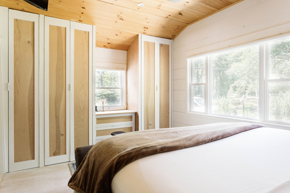 Immagine di una piccola camera matrimoniale country con pareti bianche, parquet chiaro, stufa a legna e pavimento bianco