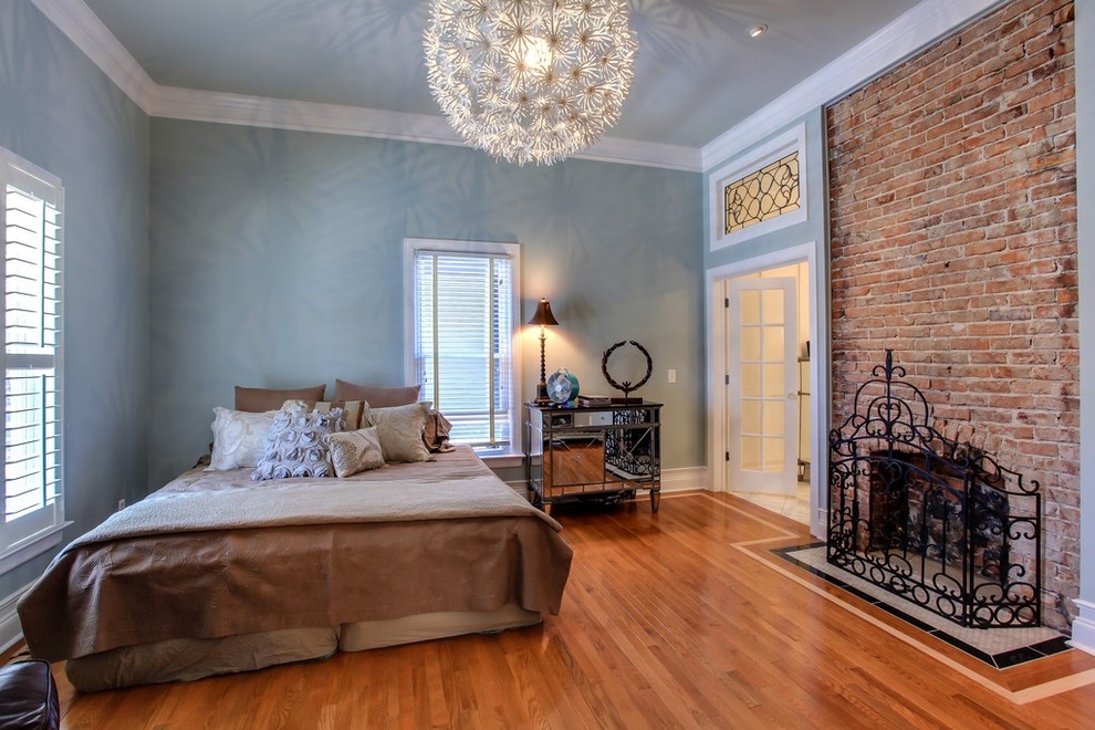 Ejemplo de dormitorio principal clásico de tamaño medio con paredes azules, suelo de madera en tonos medios, todas las chimeneas y marco de chimenea de ladrillo