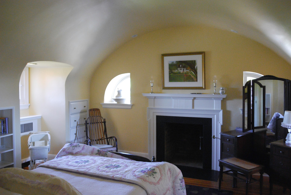 Пример оригинального дизайна: спальня среднего размера в стиле кантри с желтыми стенами, паркетным полом среднего тона, стандартным камином и фасадом камина из дерева