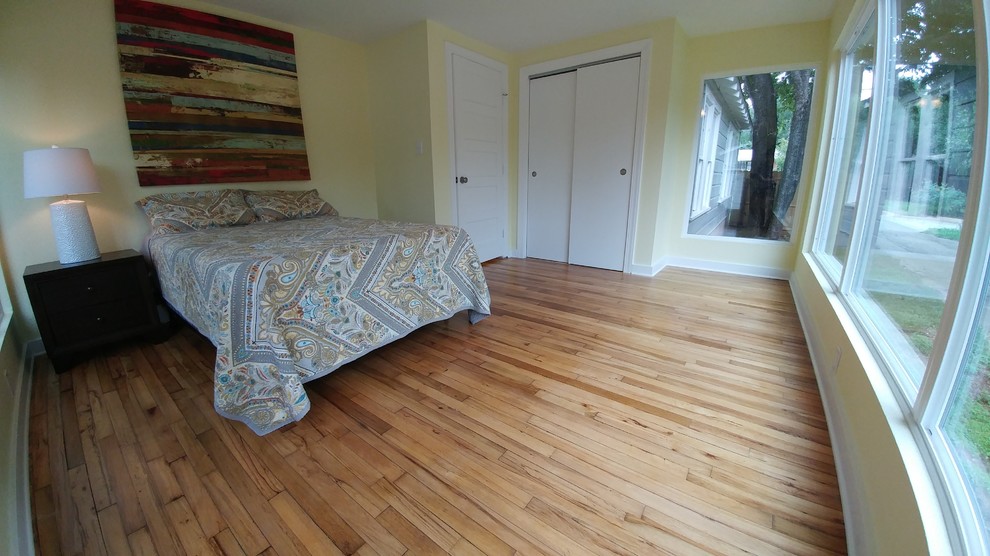This is an example of a classic bedroom in Austin with yellow walls and light hardwood flooring.