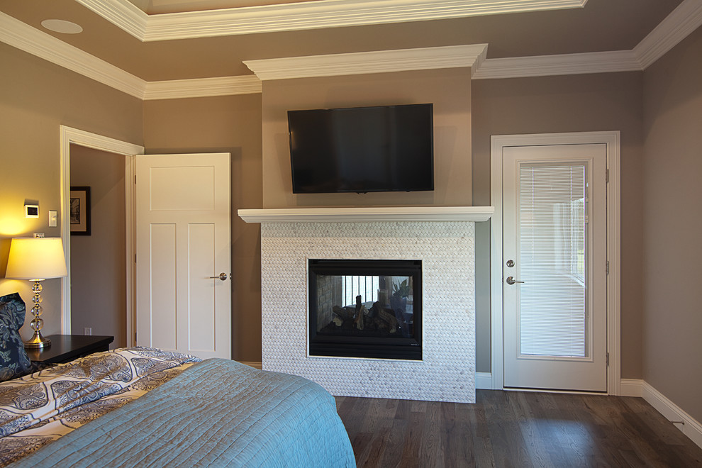 Diseño de dormitorio principal tradicional grande con paredes grises, suelo de madera en tonos medios, marco de chimenea de baldosas y/o azulejos y chimenea de doble cara