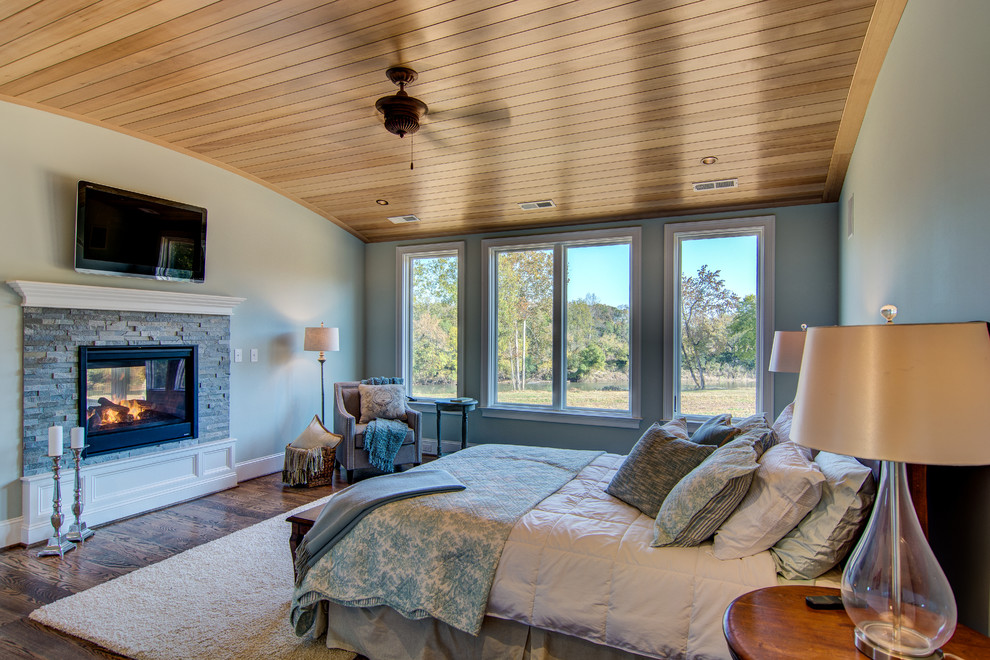 Idée de décoration pour une très grande chambre parentale tradition avec un mur bleu, un sol en bois brun, une cheminée double-face et un manteau de cheminée en pierre.