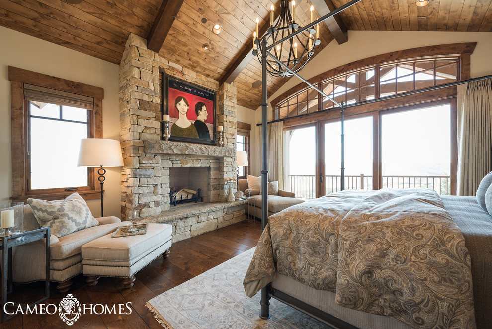 Diseño de dormitorio principal rural grande con paredes blancas, suelo de madera en tonos medios, todas las chimeneas y marco de chimenea de piedra