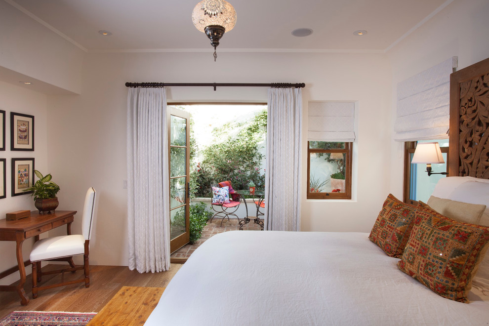 Modelo de habitación de invitados mediterránea grande sin chimenea con suelo de madera en tonos medios y paredes blancas