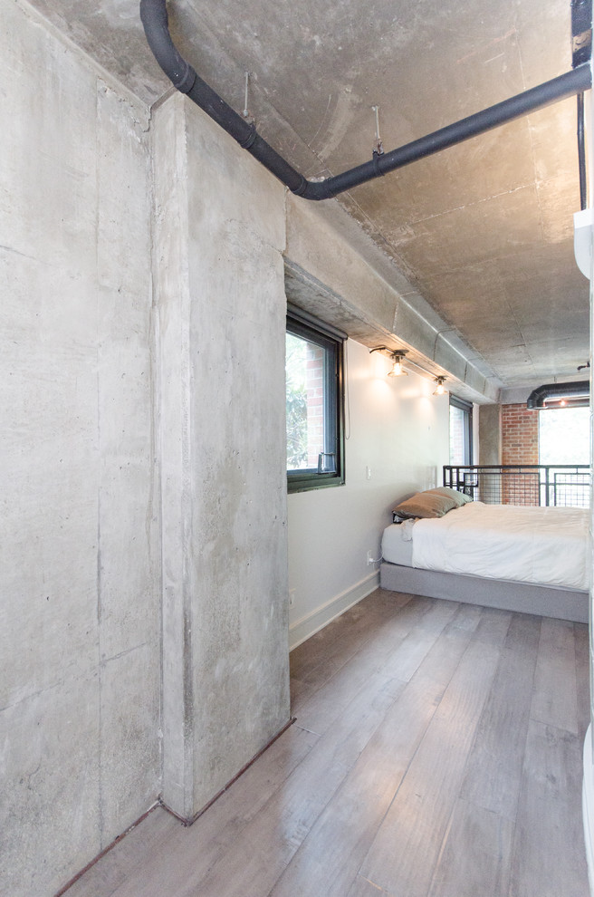 Imagen de dormitorio tipo loft urbano de tamaño medio con suelo de cemento, paredes blancas y suelo marrón