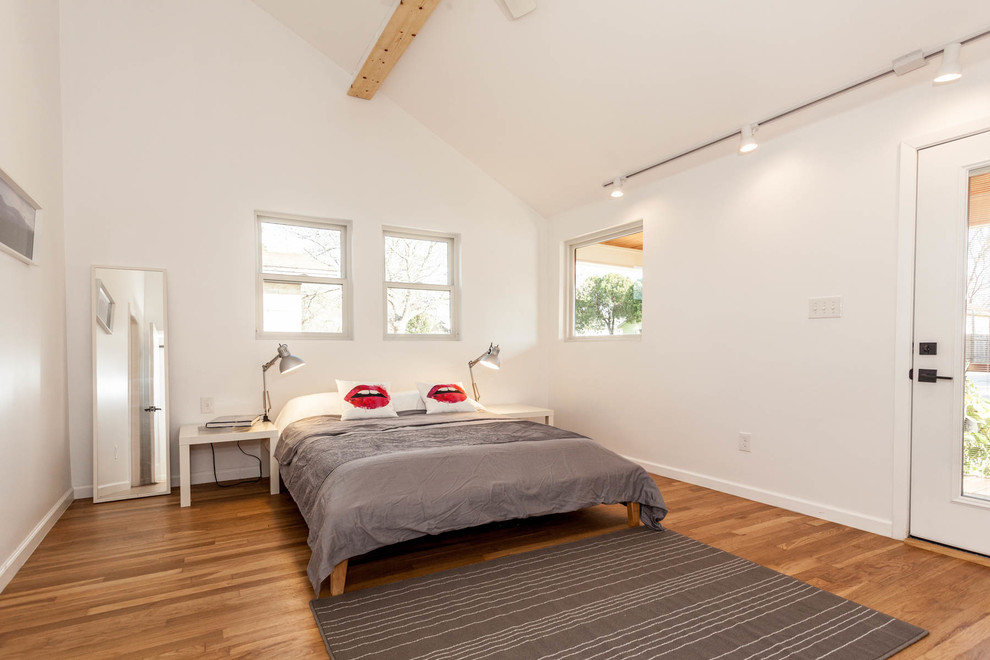 Contemporary bedroom in Austin with white walls and medium hardwood flooring.
