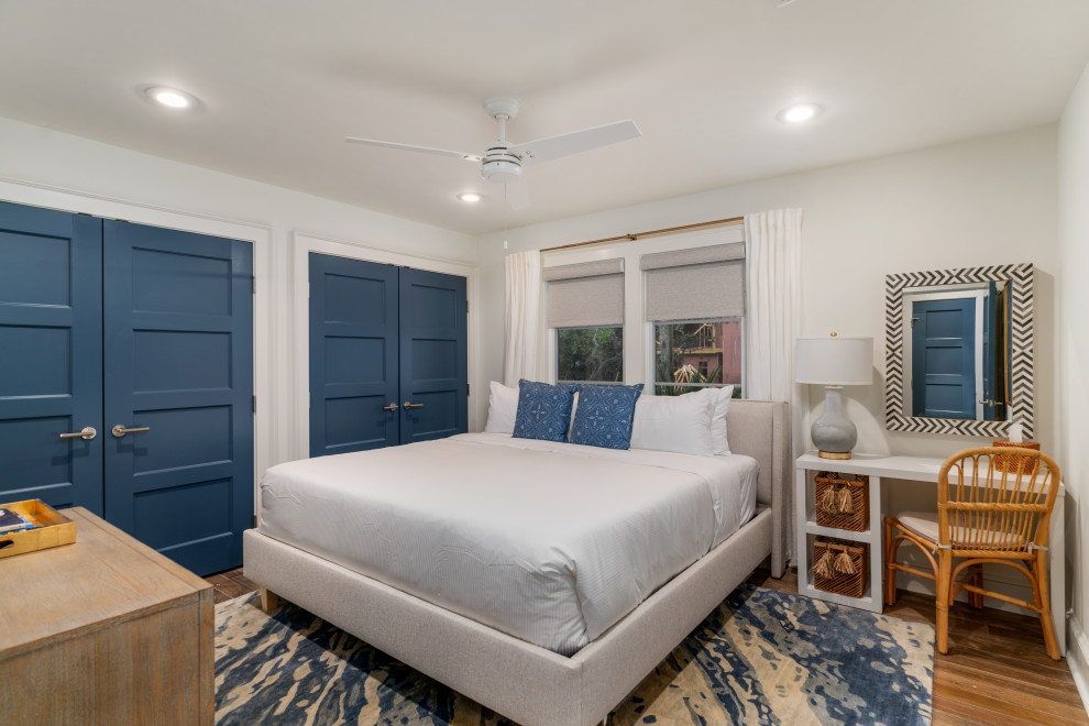 Diseño de dormitorio costero de tamaño medio con paredes blancas, suelo de madera en tonos medios, chimenea de doble cara, marco de chimenea de yeso y suelo gris