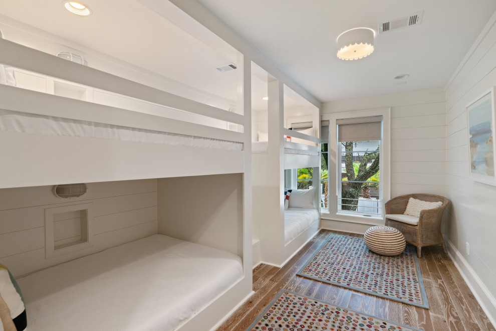 Foto de dormitorio costero de tamaño medio con paredes blancas, suelo de madera en tonos medios, chimenea de doble cara, marco de chimenea de yeso y suelo gris