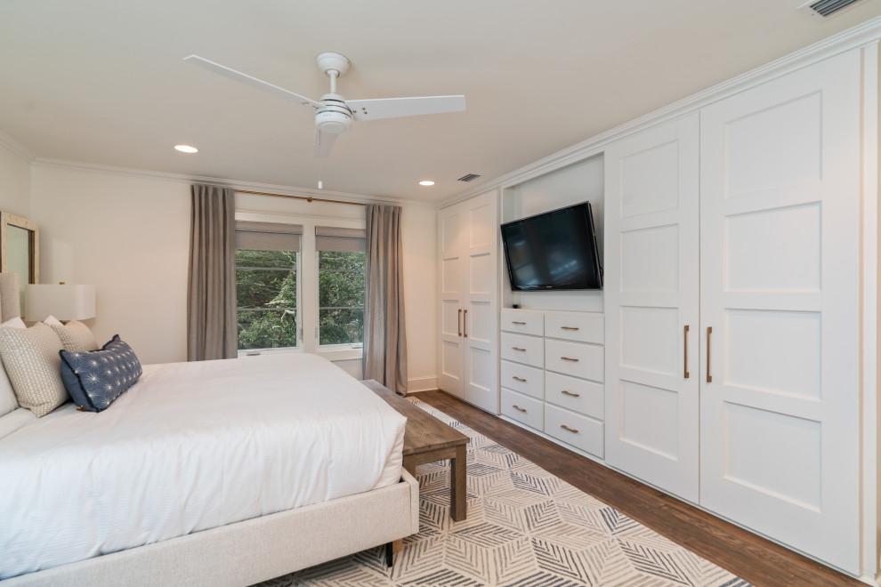 Diseño de dormitorio costero de tamaño medio con paredes blancas, suelo de madera en tonos medios, chimenea de doble cara, marco de chimenea de yeso y suelo gris